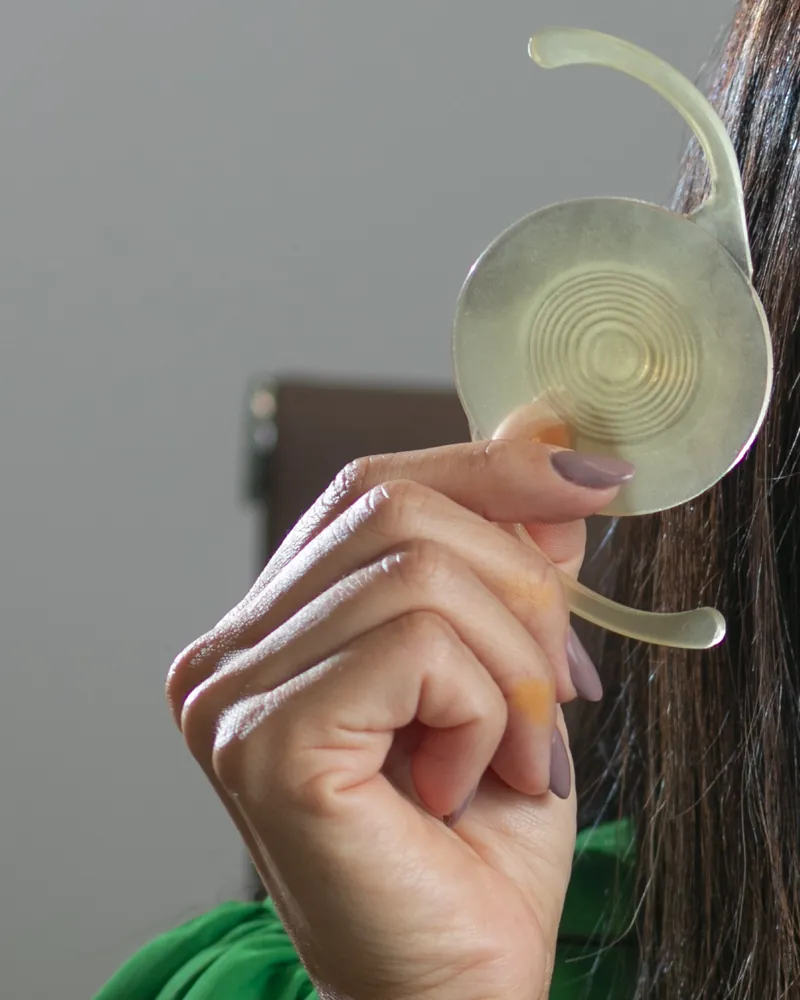 Lente intraocular segurada entre os dedos, em primeiro plano
